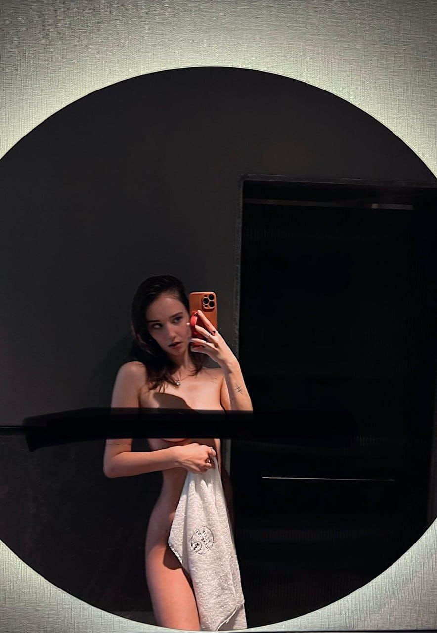 Dimly lit mirror selfie with a white towel wrapped around the lower body, standing before a circular mirror.