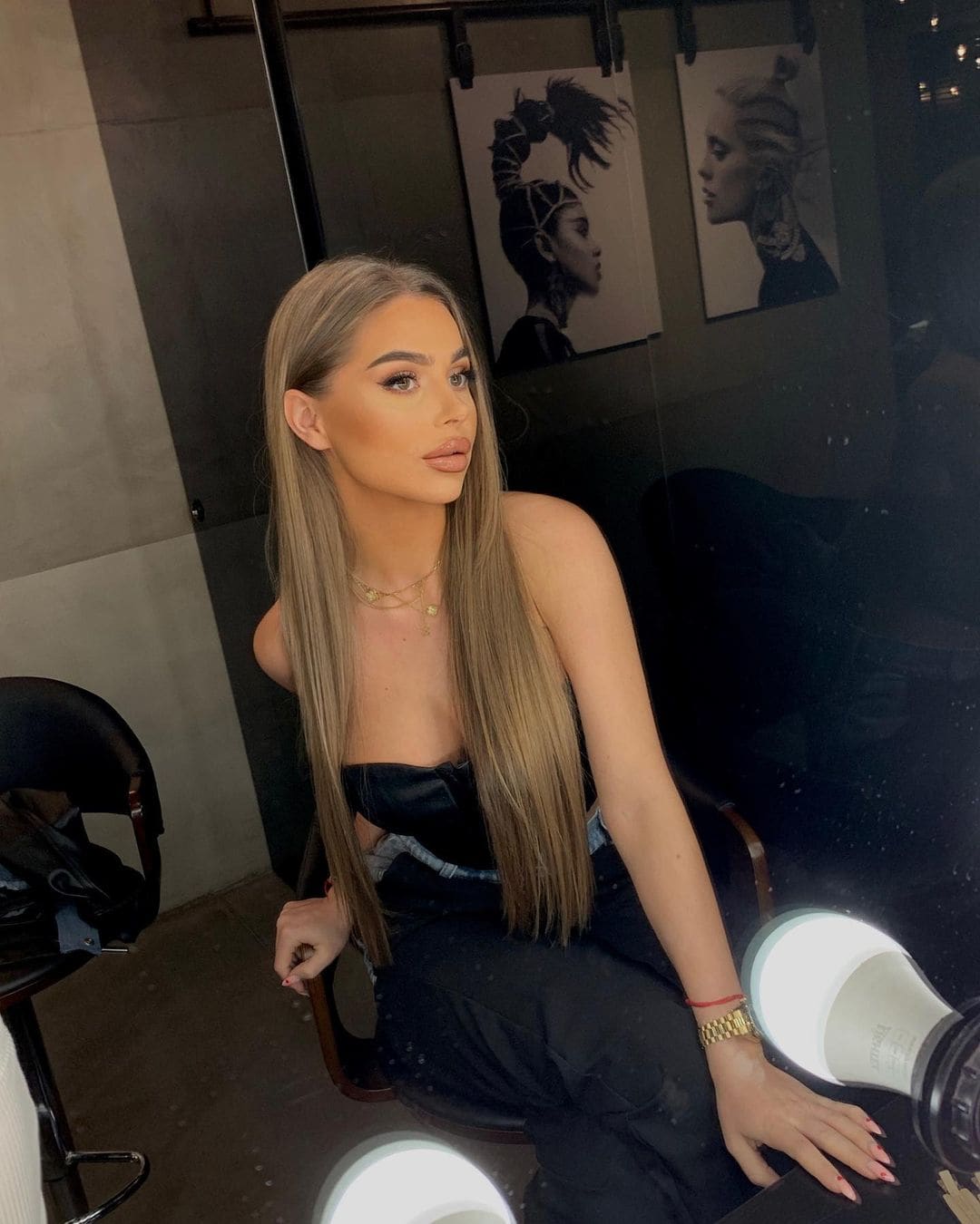 Lida sits in a chair wearing a black strapless top and dark pants, with framed black-and-white portraits on the wall behind her.