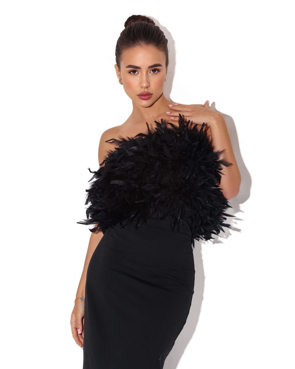 Silvia stands against a white background in a strapless black dress with a feathered bodice, her left hand resting on her shoulder.